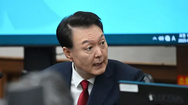 Former South Korean president Yoon Suk Yeol seated in court with a blue background