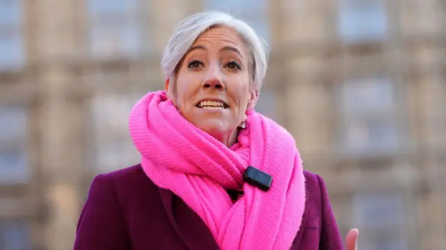 Cooper wears a pink scarf has she speaks to media outside Westminster