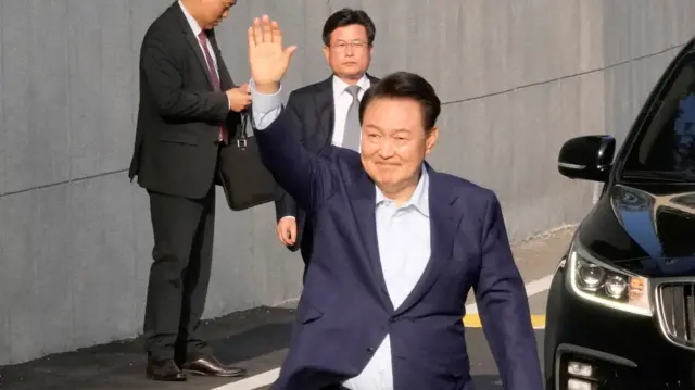 Former South Korean president Yoon Suk Yeol waving with security and a black car in the background