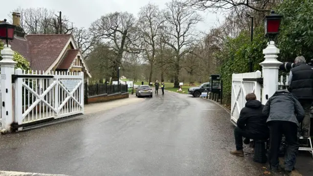 Several people are seen crouching over next to a white gate close to Royal Lodge