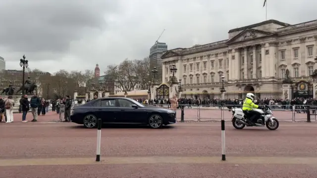 A black car with a police motorcycle driving in front