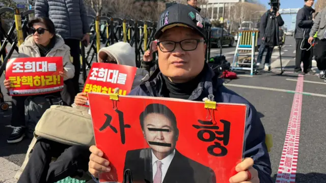 Park holding a sign with Yoon's face and the words "execute"