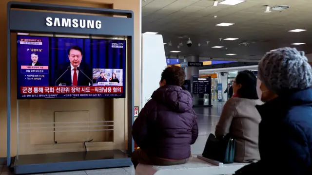 People sit and watch court verdict on TV screen in Seoul