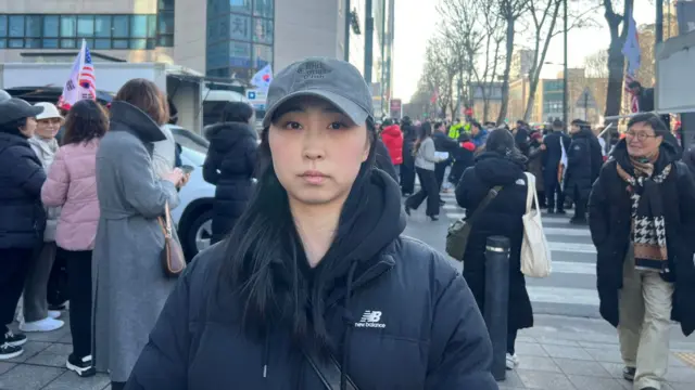 A woman wears a dark jacket and baseball cap