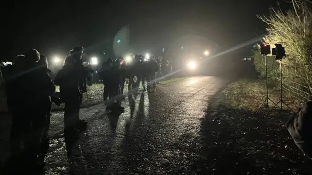 A line of photographers along a dark, rural road.