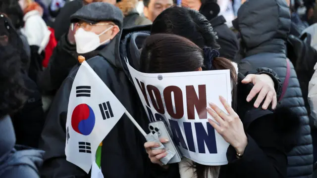 A woman holds a sign over her face and a Korean flag in her other hand