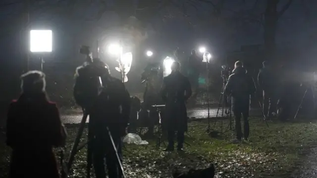 Journalists standing in the dark with lights and cameras on them.