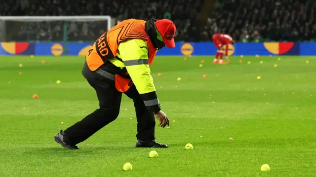Steward picks up balls on the Celtic Park pitch