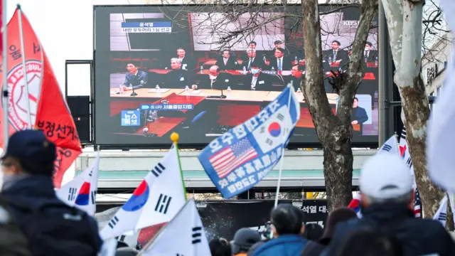 People wave flags in front of huge screen in Seoul which displays the court's verdict