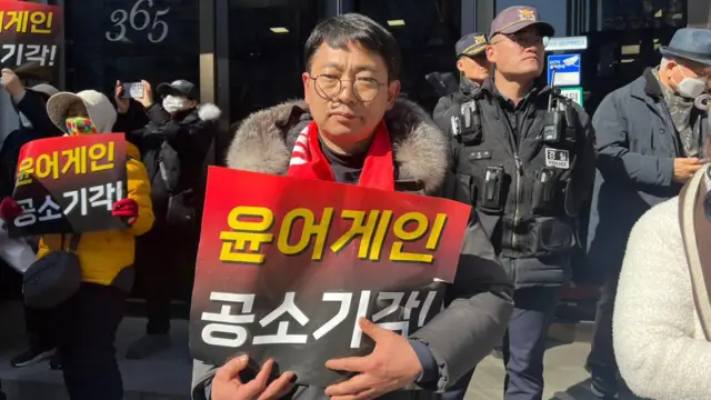 A man holding a sign with Korean words and looking into the camera
