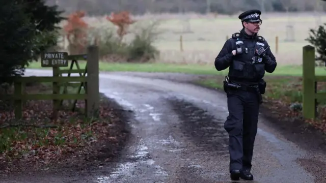 A police officer stands by a wooden gate near a sign saying "private no entry"