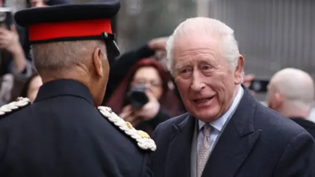 King Charles smiles as he greets someone in uniform
