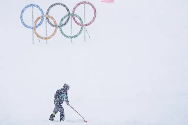 A member of staff displaces excess snow under heavy snowfall ahead of the men and women's sprint ski mountaineering semi-finals