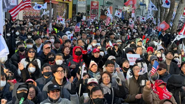 A large crowd on Yoon's supporters gather outside, some waving US and South Korea national flags