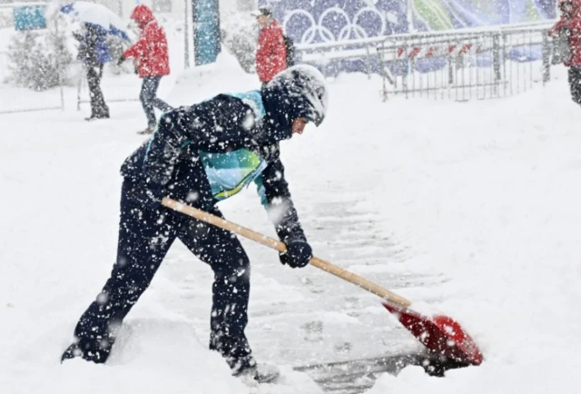 A volunteer clears snow outside the Cortina Curling