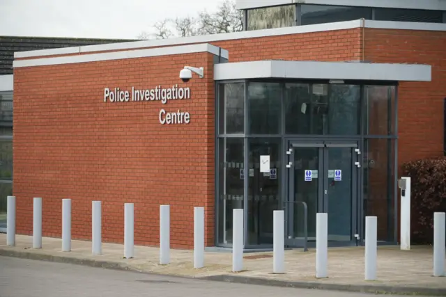View of building exterior. Writing on the wall reads: "Police Investigation Centre"