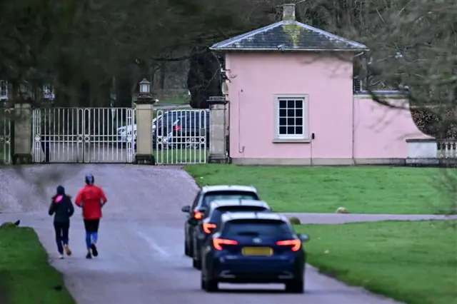 Three black cars drive towards a gate at Royal Lodge