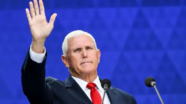 Former vice president Mike Pence at a lectern raising his hand