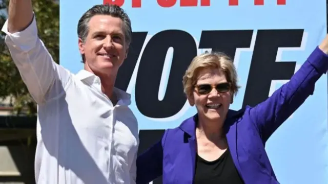 Newsom and Warren with an arm around each other, raising their hands and smiling