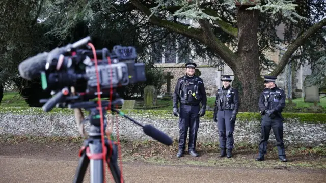 Police officers stand outside Wood Farm, Sandringham, next to a camera on a tripod