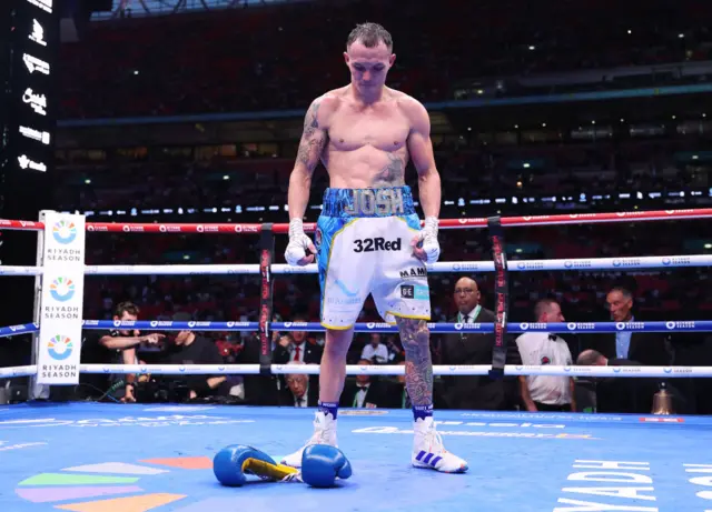 Josh Warrington stands in a boxing ring and looks down at his gloves on the floor