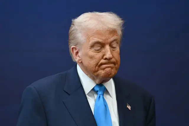 Trump, wearing a blue suit over a white shirt and blue tie, in thinking face.