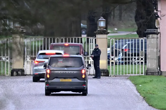 Three cars drive toward a gate at Royal Lodge