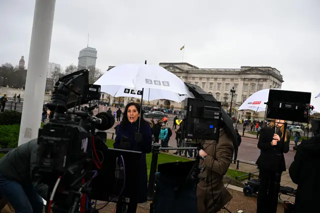 A BBC journalist stands outside Buckingham Palace
