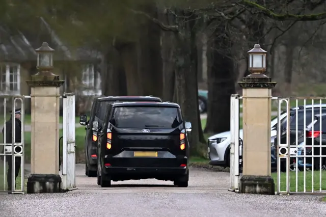 Two black cars drive through a gate at Royal Lodge