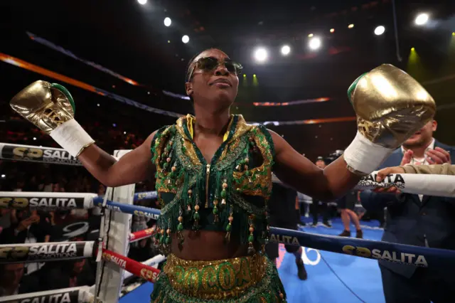 Claressa Shields wearing a green and gold vest and shorts and has gold boxing gloves