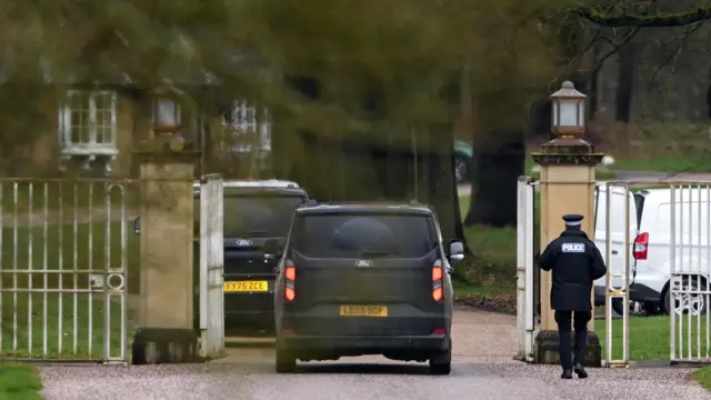 Two black Ford SUVs are seen entering a gated property, with a police officer seen walking alongside them.