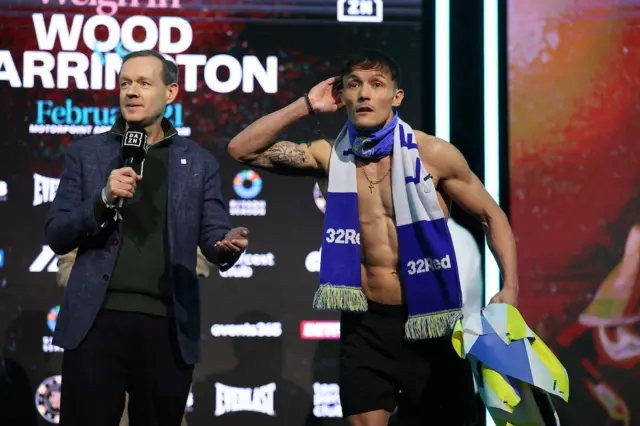 Josh Warrington cups his ear and is wearing a Leeds United scarf around his neck
