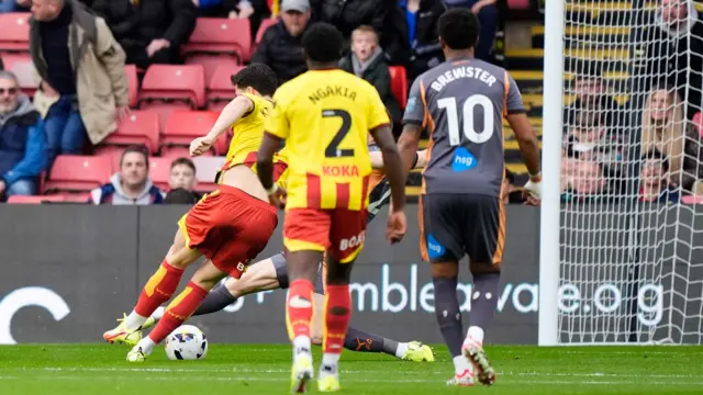 Luca Kjerrumgaard (left) kicks the ball past Derby keeper who stretches his right leg to try and stop it