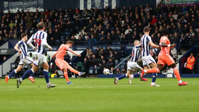 Jack Rudoni (second left) holds his leg out after striking the ball, which hovers in the air as players from both sides run in front o fit