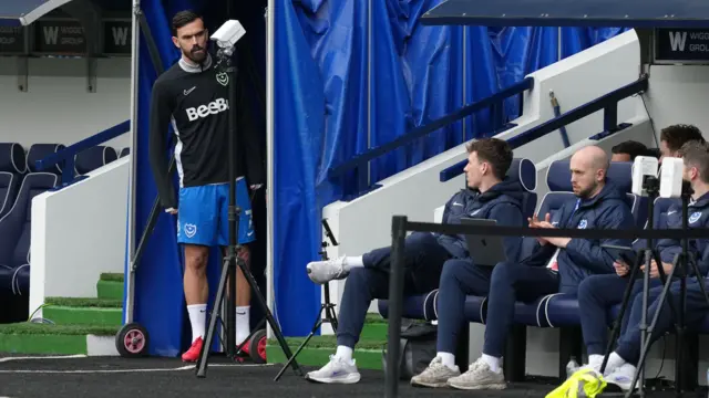 A Portsmouth player stands at the side of the dugout where coaches and players sit