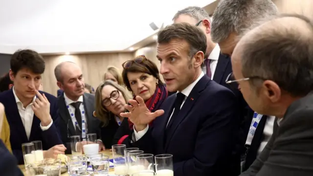 French President Emmanuel Macron raises his left hand as he speaks at an agricultural fair in Paris