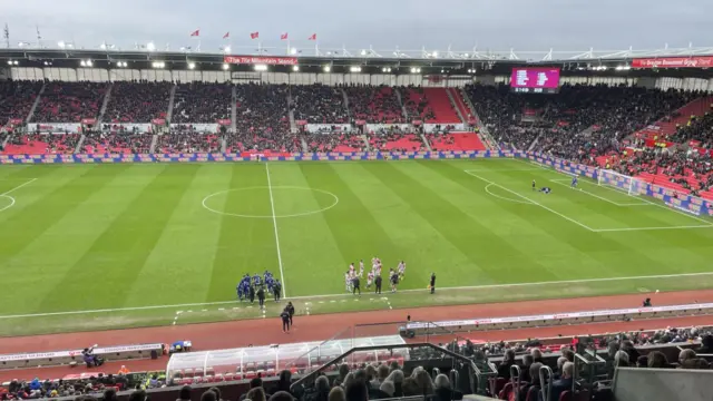 A view of Stoke's pitch and stadium from the stands, with Leicester players huddled by the dugout with manager Gary Rowett