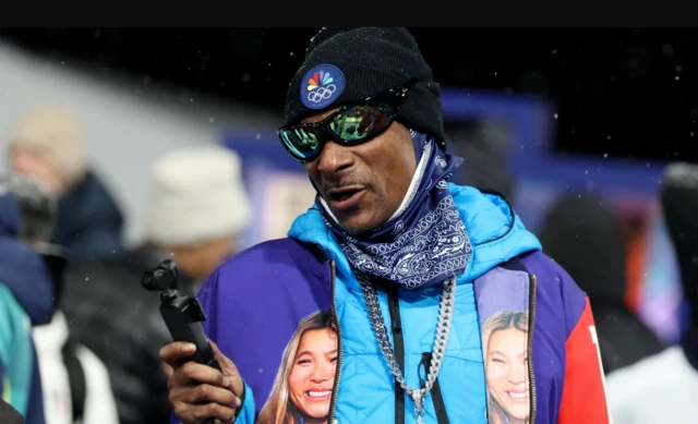 Rapper Snoop Dogg watching on wearing a jacket in team colours with a picture of Chloe Kim on each side of the jacket