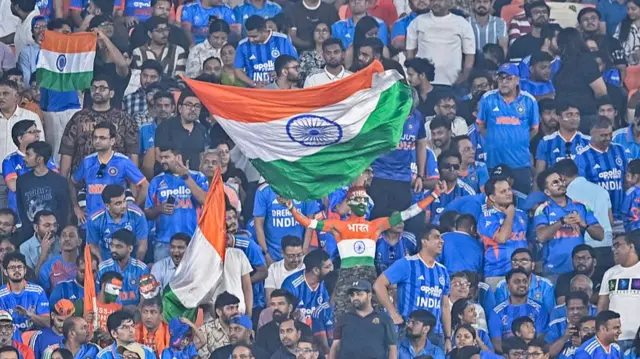 An Indian fan waving the national flag cheers from the stands