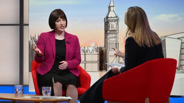 Education Secretary Bridget Phillipson wearing a pink blazer and black dress. She sits on a red chair in the BBC studio as she sits opposite Laura Kuenssberg.