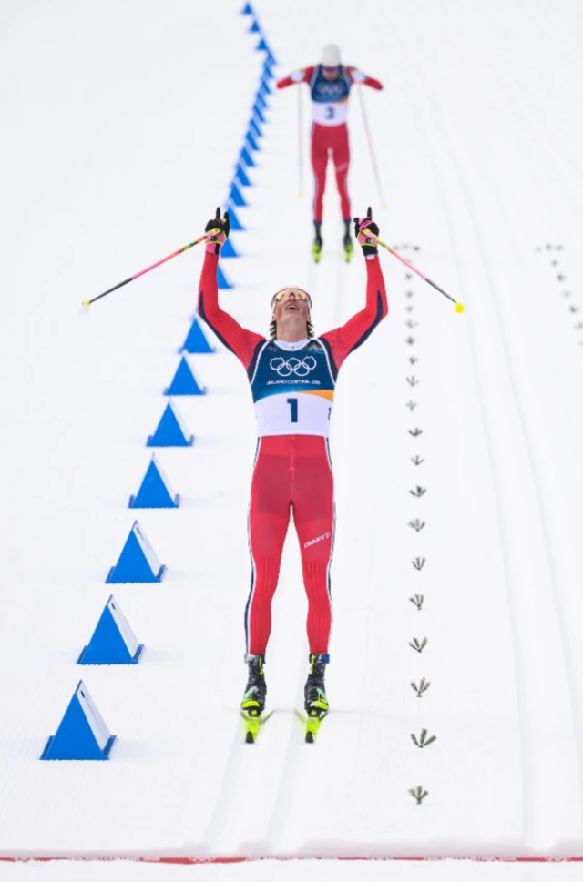 Skier raises his arms and looks to the sky in celebration at finishing a race