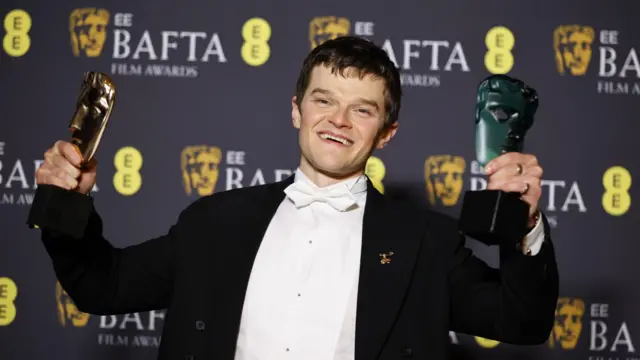 Robert Aramayo in a tuxedo shows his two Bafta awards