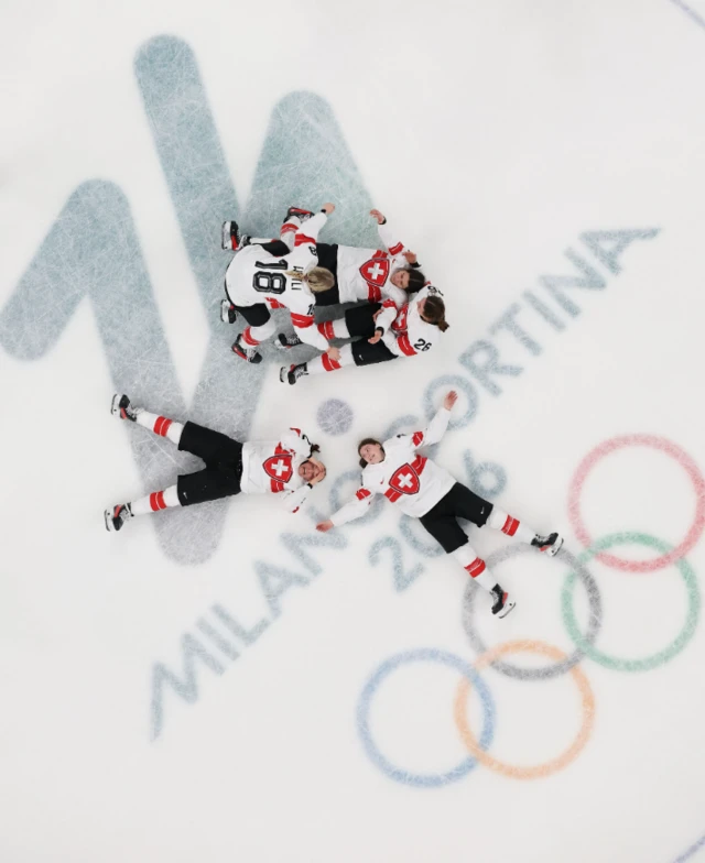 Birdseye view of five hockey players laid flat on their backs on ice having won their bronze medal match