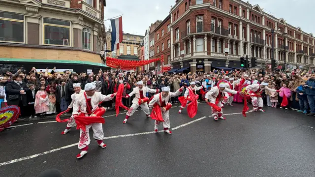 A group of dancers perform with drums, surrounding by a crowd of spectators