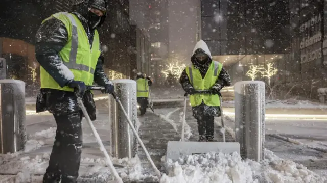 Workers in high-vis jackets clearing snow from the street in New York City