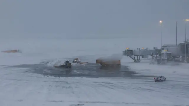 Snow ploughs on the tarmac at LaGuardia airport. You can hardly see them through the snowy conditions.