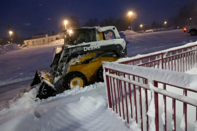 A skid-steer loader clears snow during a winter storm at the Manhasset transportation station in Manhasset, New York