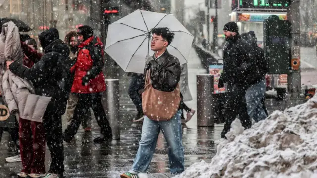 A man holding a white umbrella walking through New York as snow falls