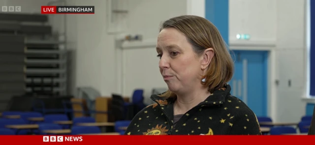 Laura Jerram wears a black blouse with yellow stars as she speaks to a BBC News journalist at a school