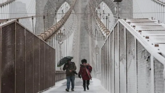 Two people walk across the Brooklyn Bridge in the snow